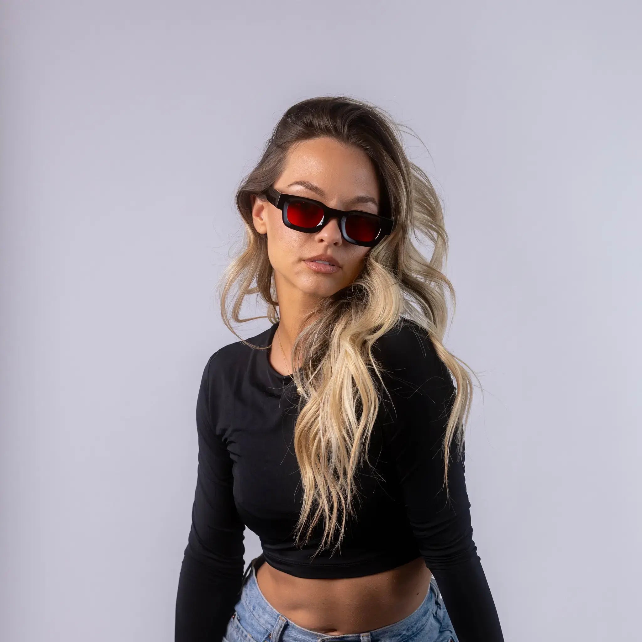 A female model wearing Exposure Sunglasses polarized sunglasses with black frames and red lenses, posing against a white background.