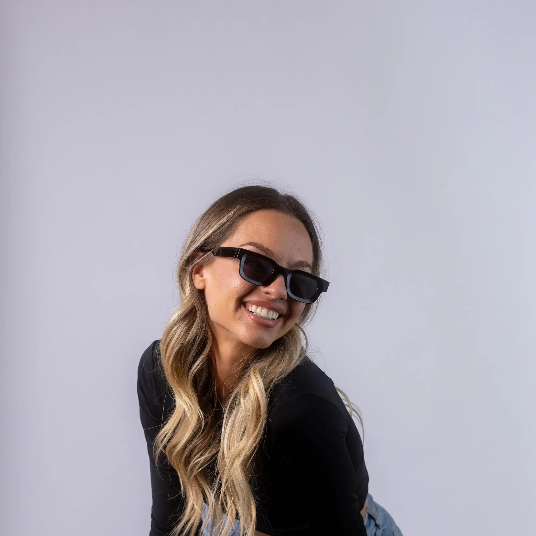 A female model wearing Exposure Sunglasses polarized sunglasses with black frames and black lenses, posing against a white background.