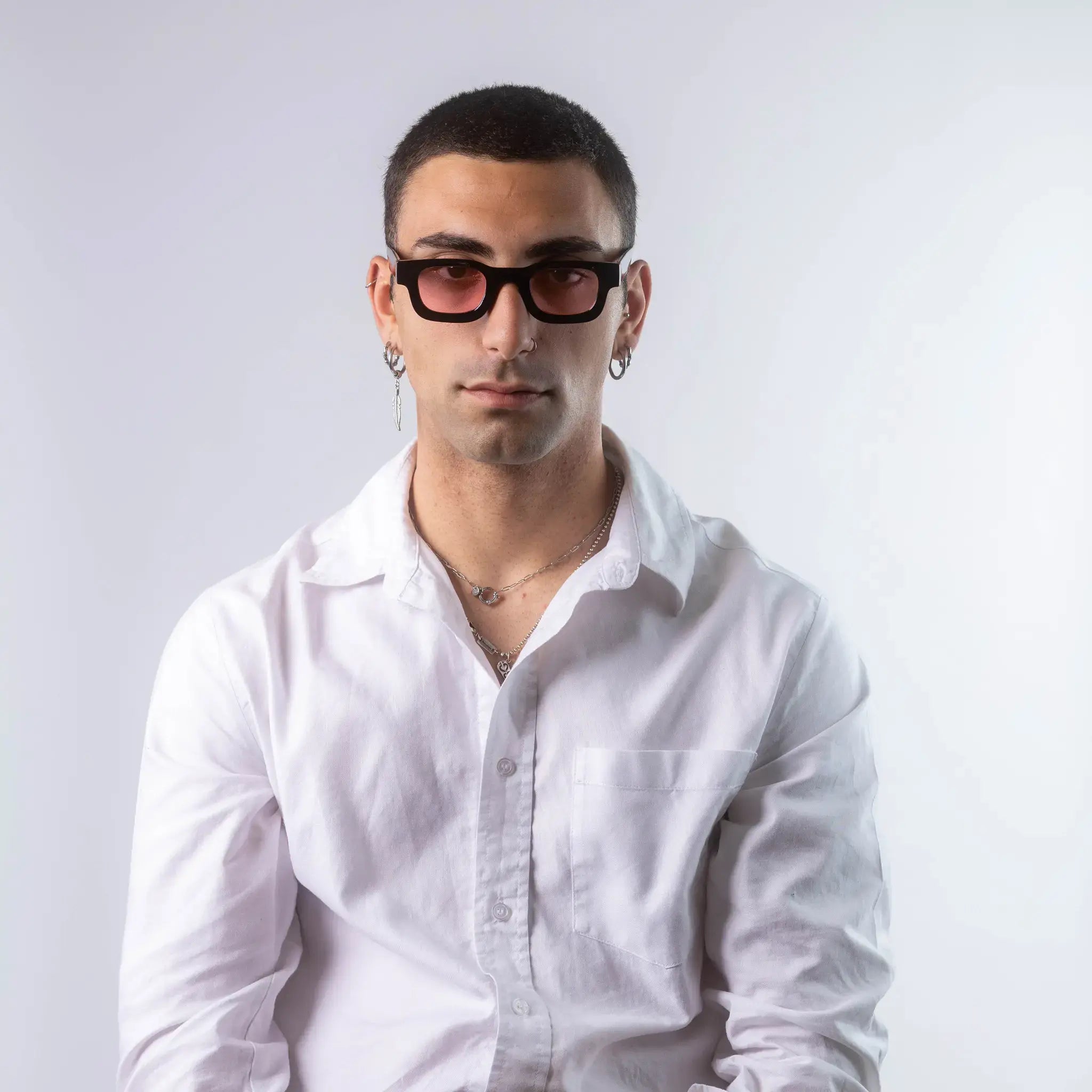 A male model wearing Exposure Sunglasses polarized sunglasses with black frames and pink lenses, posing against a white background.