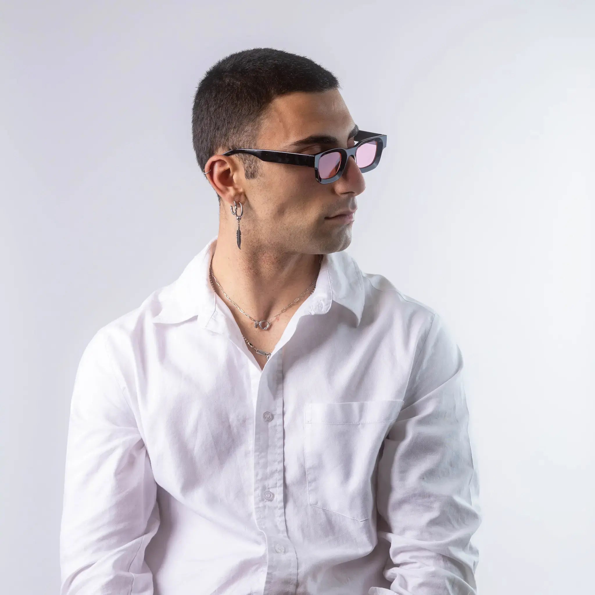 A male model wearing Exposure Sunglasses polarized sunglasses with black frames and pink lenses, posing against a white background.