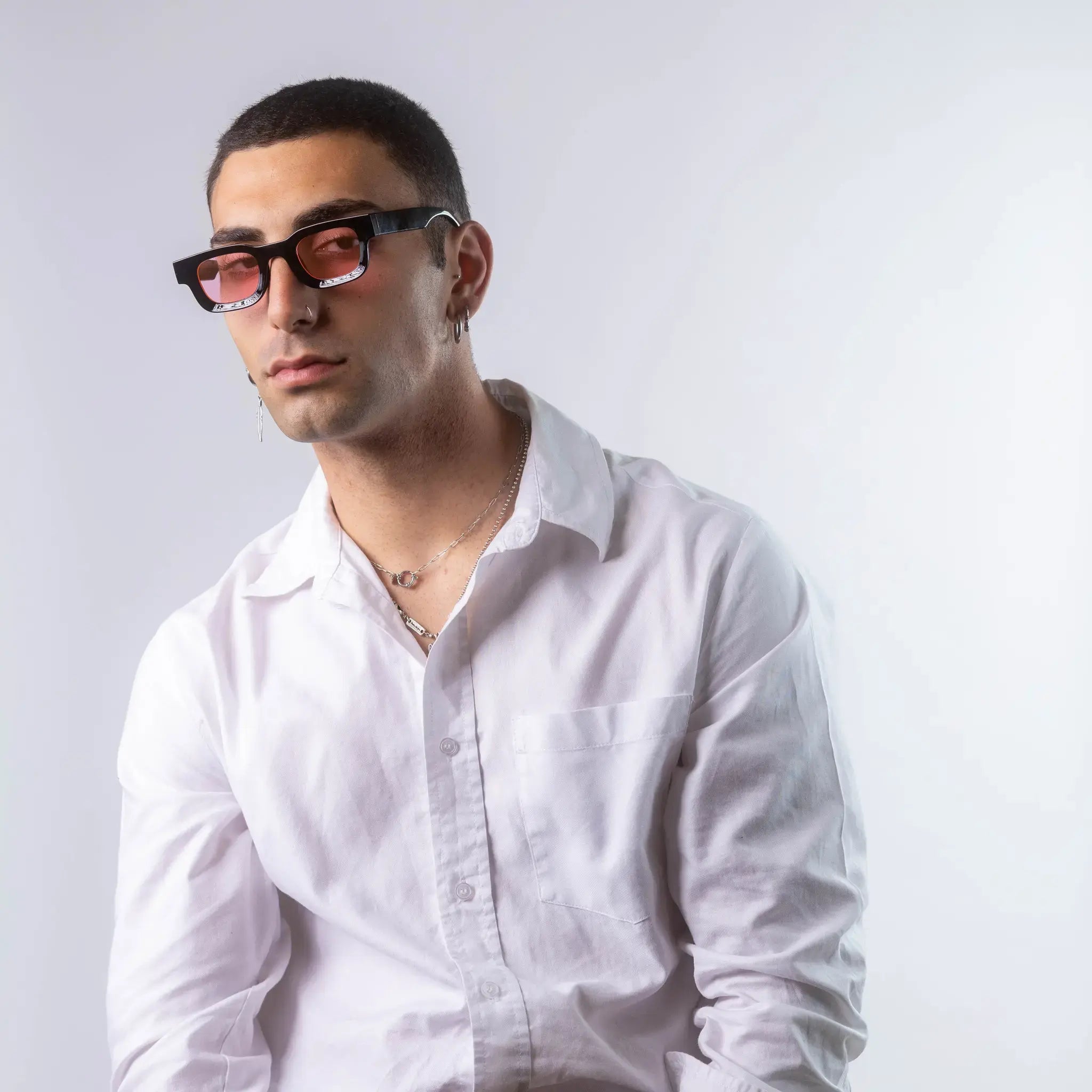 A male model wearing Exposure Sunglasses polarized sunglasses with black frames and pink lenses, posing against a white background.